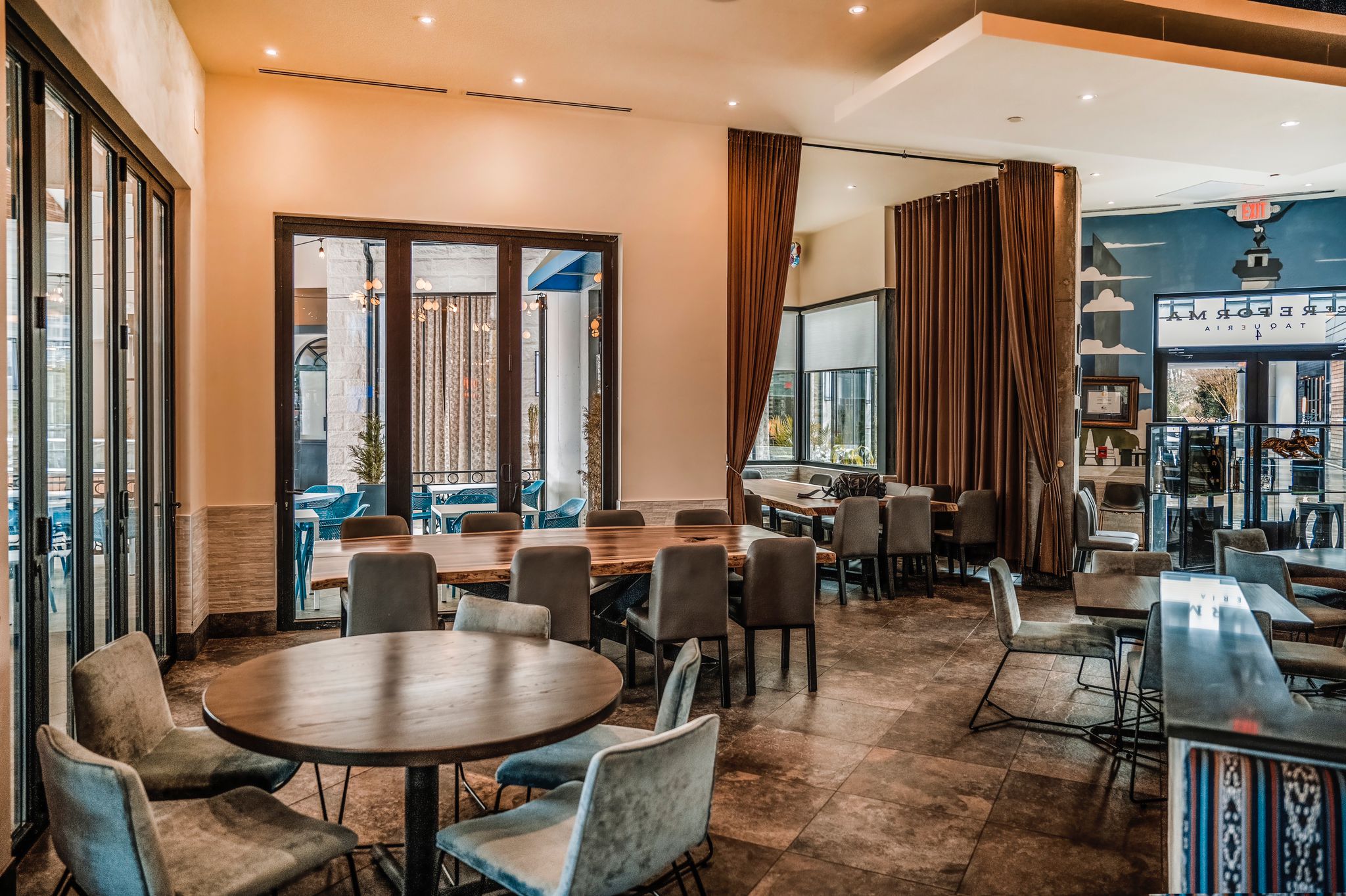 This section is cozy yet connected to the rest of the restaurant. The natural light streaming through the large windows highlights the clean lines and earthy tones of the furnishings