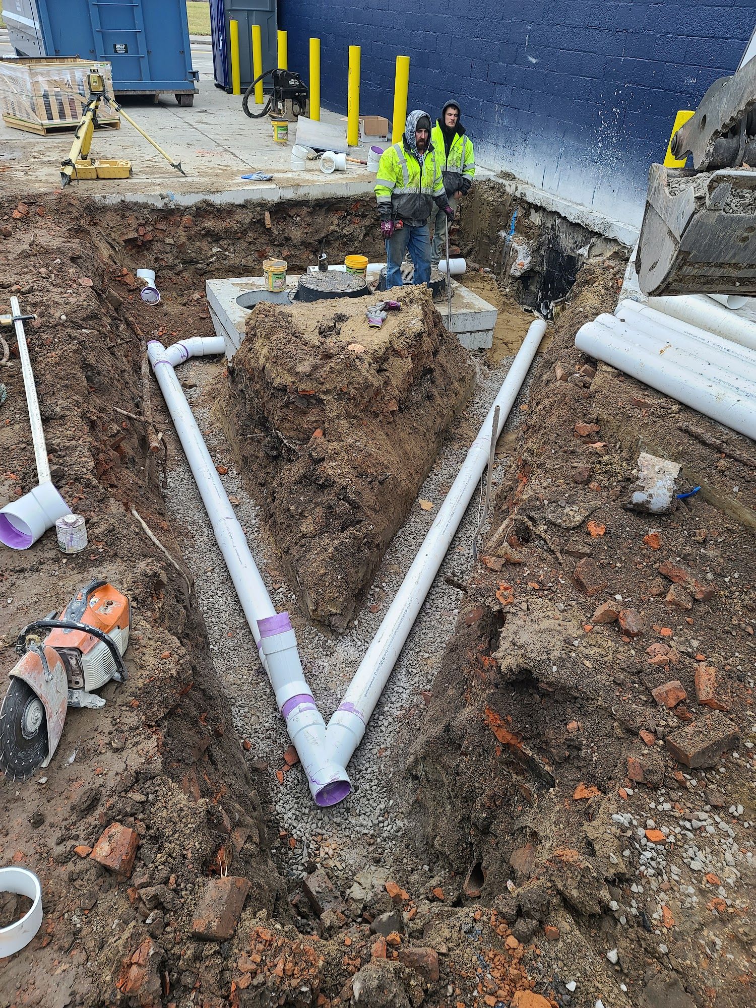 Workers install PVC drainage piping connected to a concrete catch basin near a commercial building. The system manages site runoff and supports long-term stormwater control.