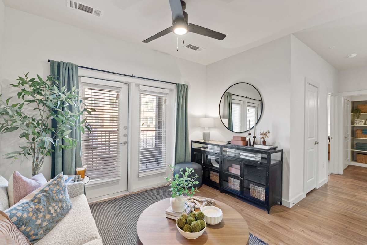 A living room with a couch, a table, a plant, and a mirror. 