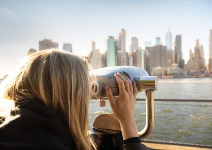 Une femme regardant la ligne d'horizon de New York à travers une lunette panoramique.