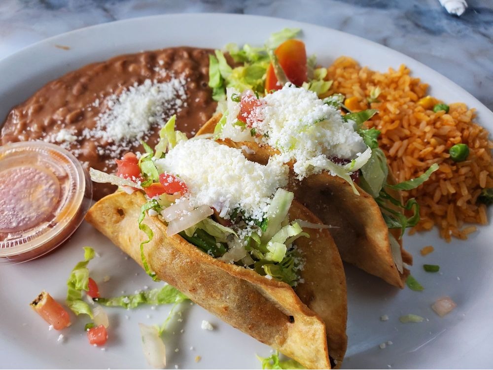 Tacos dorados plate from Yolys Mexican Kitchen, topped with lettuce, tomato, and crumbled cheese, served with Mexican rice, refried beans, and salsa.
Plato de tacos dorados de Yolys Mexican Kitchen, preparados con lechuga, tomate y queso desmoronado, acompañados de arroz mexicano, frijoles refritos y salsa.