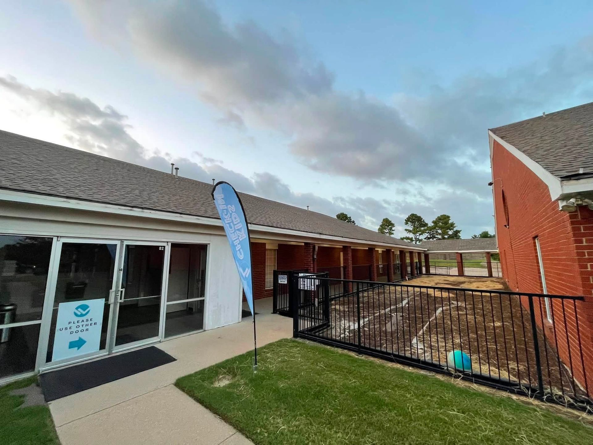 Commercial roofing project showing a brick facility with shingle roofing, glass entrance doors, fenc 