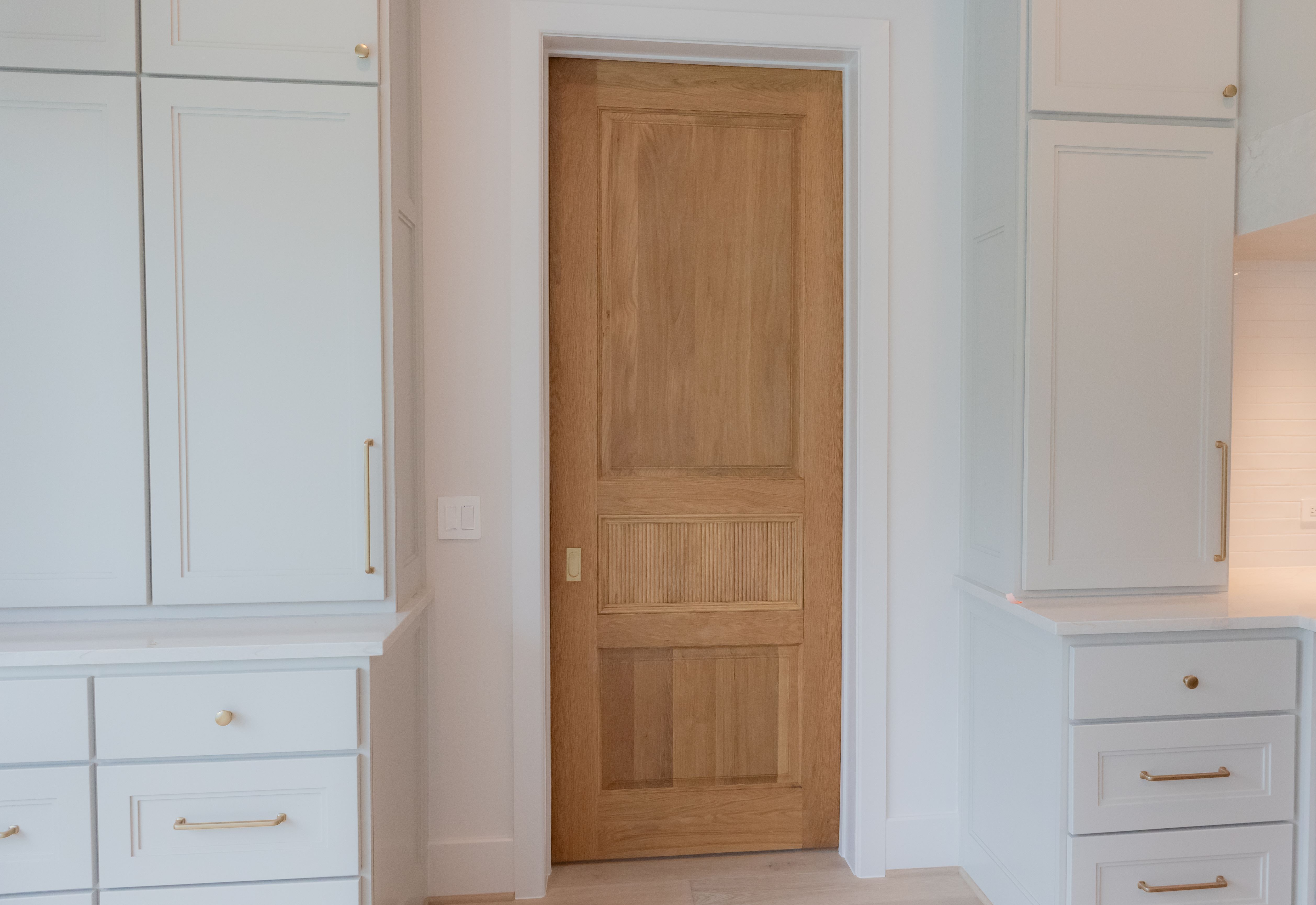 A white oak pocket door installed within a modern kitchen, framed by custom white cabinetry, highlighting the seamless blend of functionality and design.