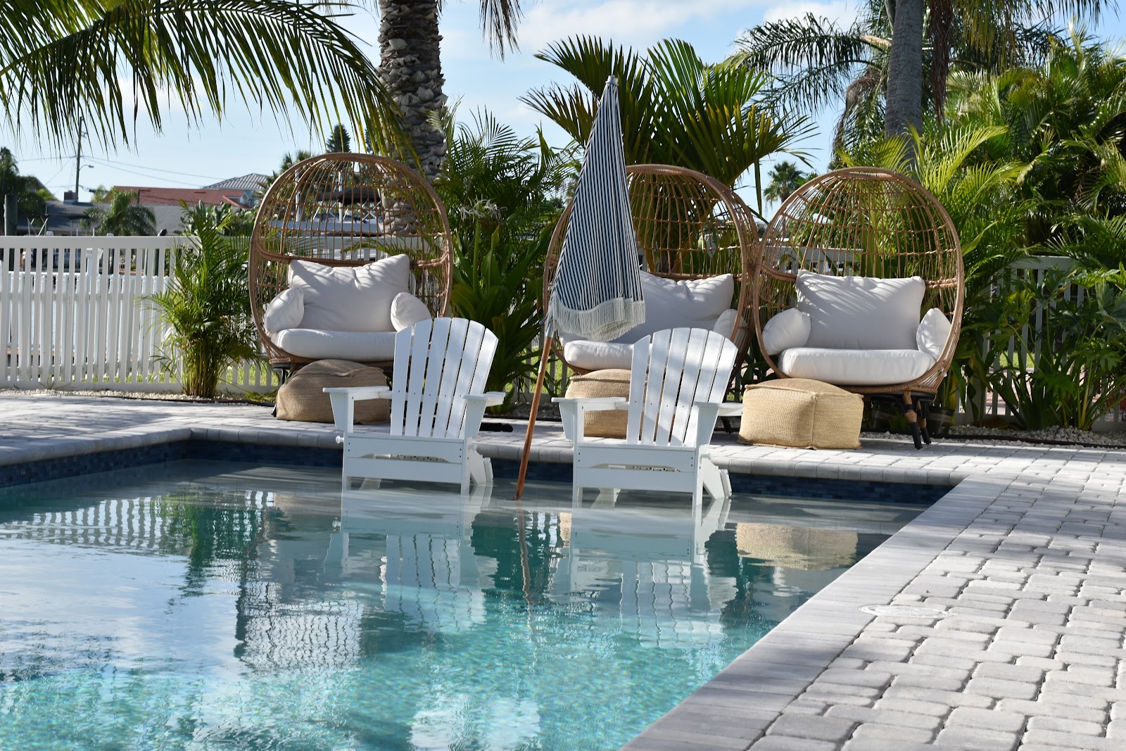 Backyard swimming pool with submerged lounge chairs, gray paver decking, tropical plants, and relaxing outdoor seating.