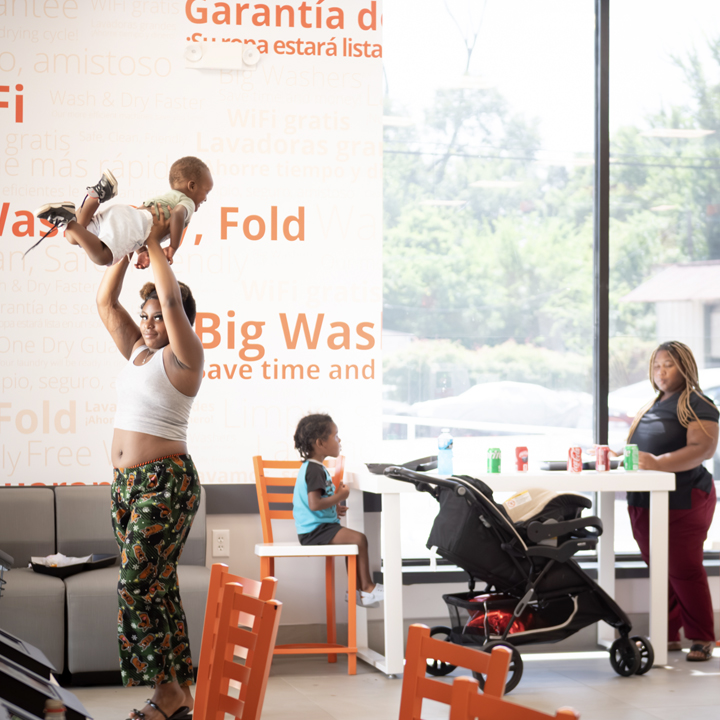 Customer and child inside a clean, welcoming Speed Queen Laundry with laundry equipment and seating  