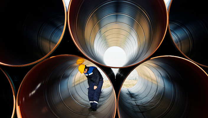 Worker in a hard hat walking through a large industrial pipe.