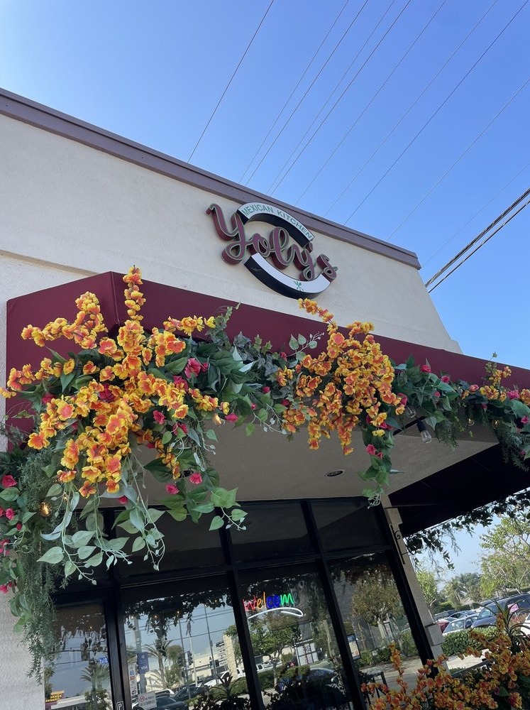Exterior of Yolys Mexican Kitchen in Downey, California, featuring the restaurant’s storefront sign, colorful floral decorations, and welcoming front entrance.
Exterior de Yolys Mexican Kitchen en Downey, California, con el letrero del restaurante, decoraciones florales coloridas y una entrada acogedora.