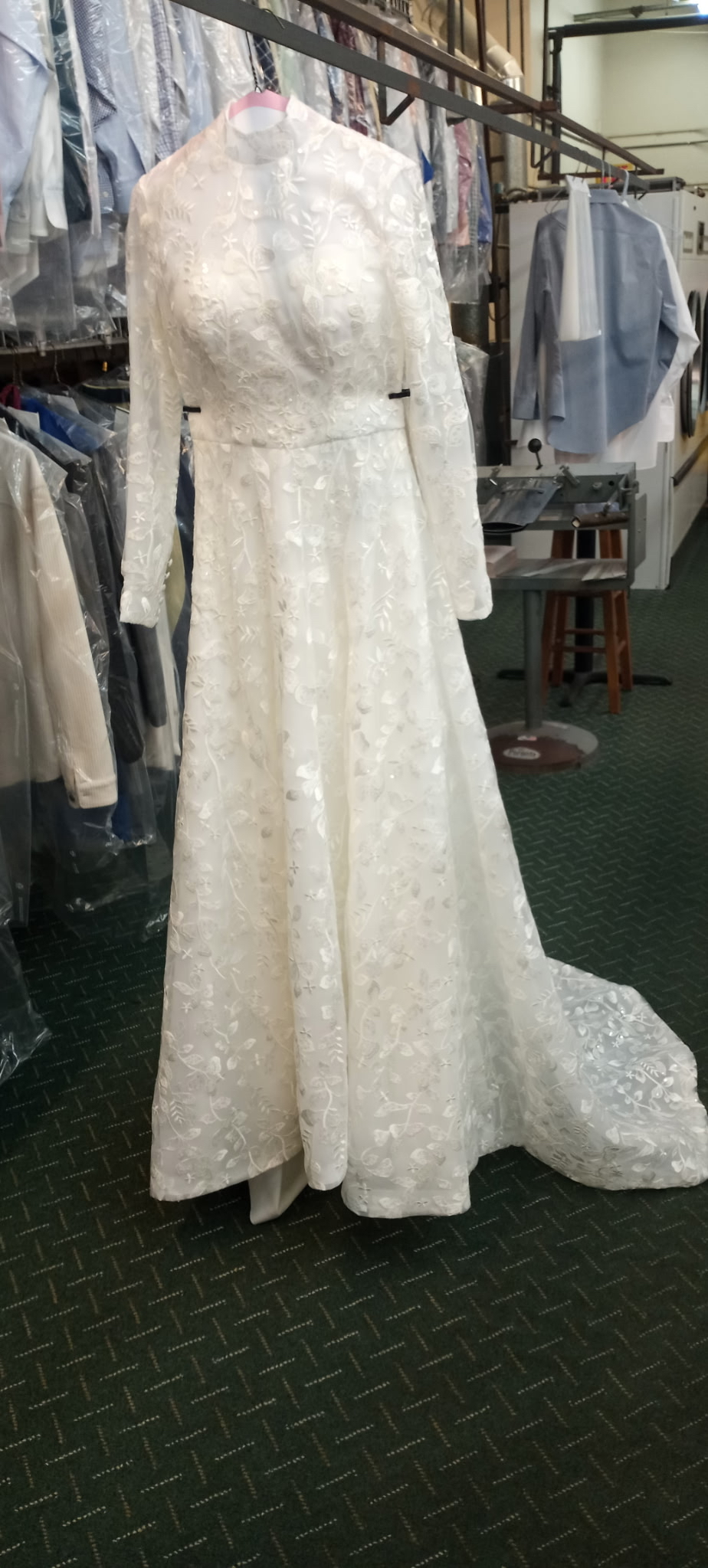 A long-sleeved, lace-overlay white wedding gown displayed on a mannequin during professional tailoring and alterations at Plaza Cleaners