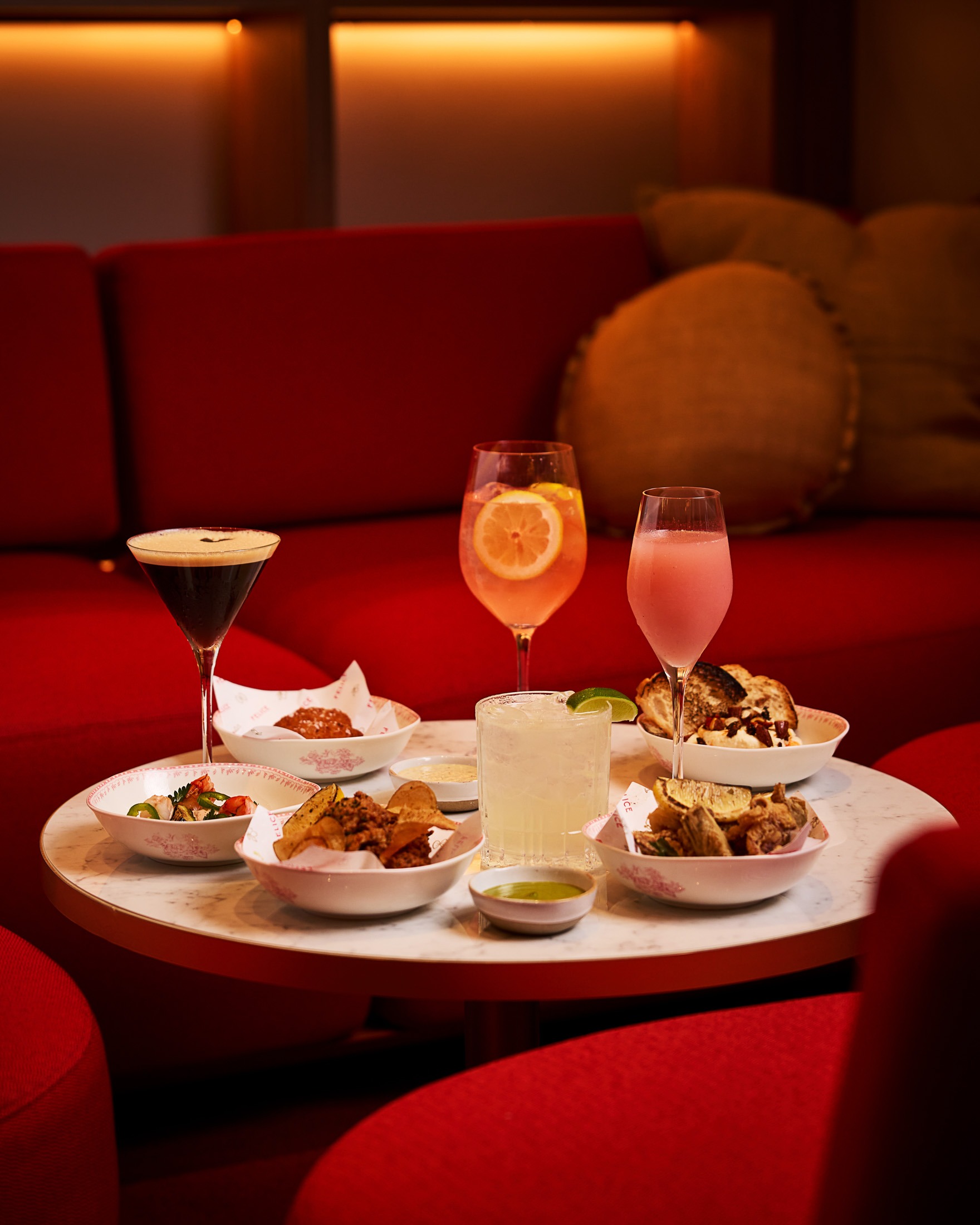 A spread of small plates including fried artichokes and calamari, paired with an espresso martini and spritz cocktails at a chic Italian lounge.
