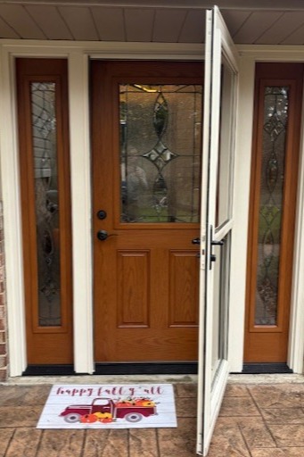 Residential front entry door system showing a wood-grain entry door with decorative glass insert and matching glass sidelights, along with an open full-view storm door. This setup provides added weather protection while preserving natural light and a welcoming entryway.