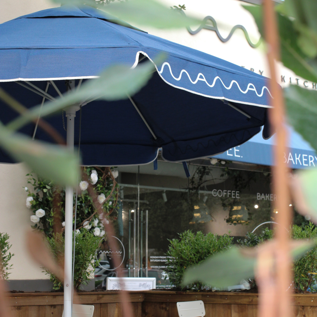 Outdoor seating at maman Park Cities features signature blue umbrellas and lush greenery, creating a 