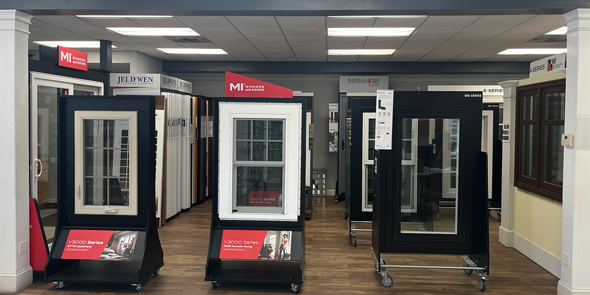 A display area at Builders FirstSource in Oxford, CT, featuring MI Windows, JELD-WEN, and other premium window options arranged on rolling stands with informative signage.