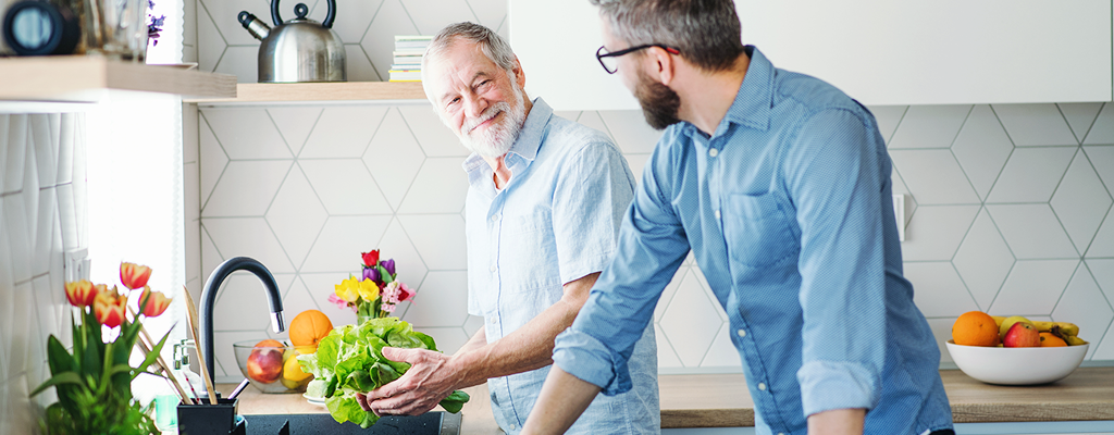Two men standing in a bright, modern kitchen washing lettuce.