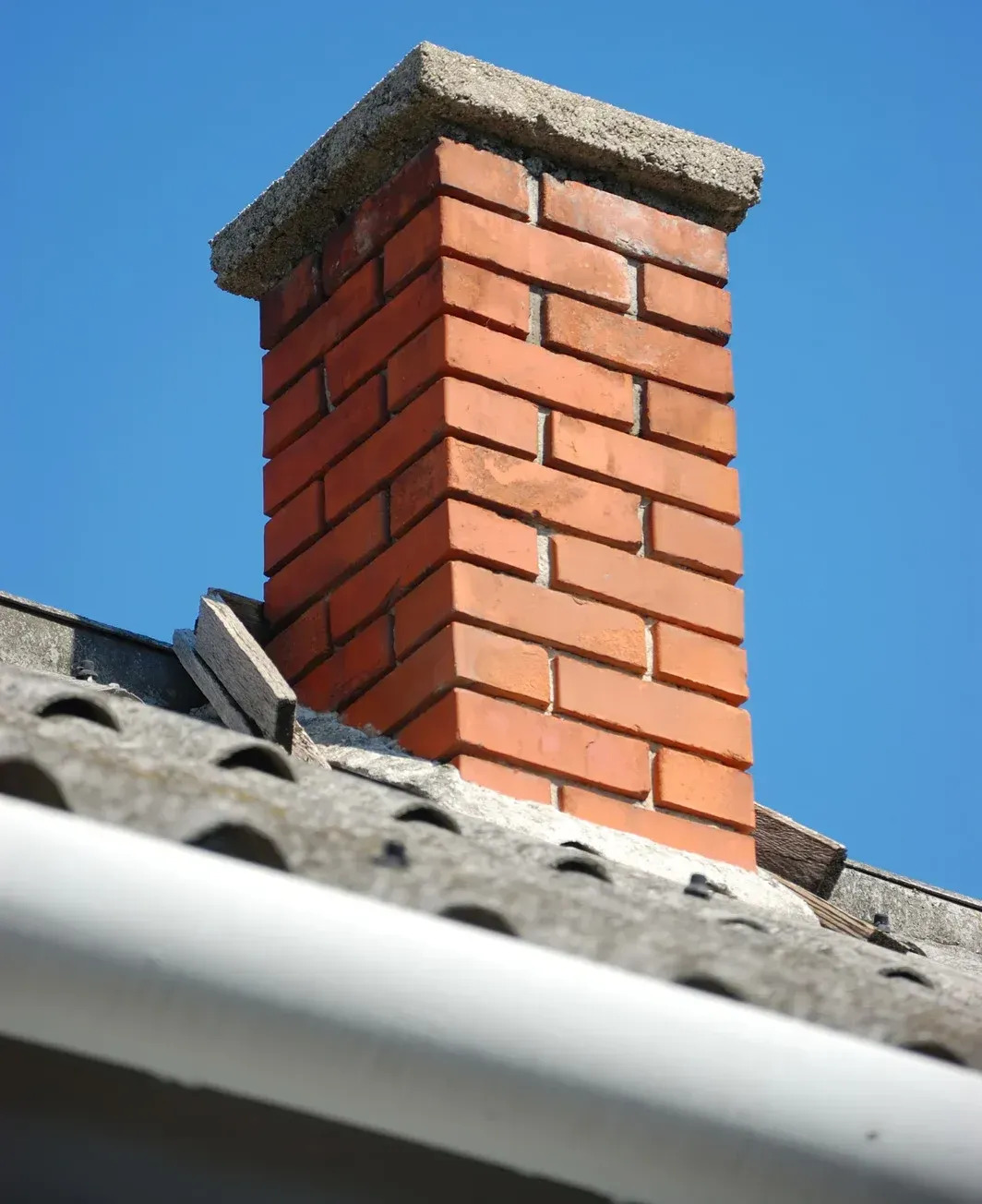 A sturdy brick chimney stands prominently on a tiled roof under a clear blue sky, highlighting classic residential architecture and construction.