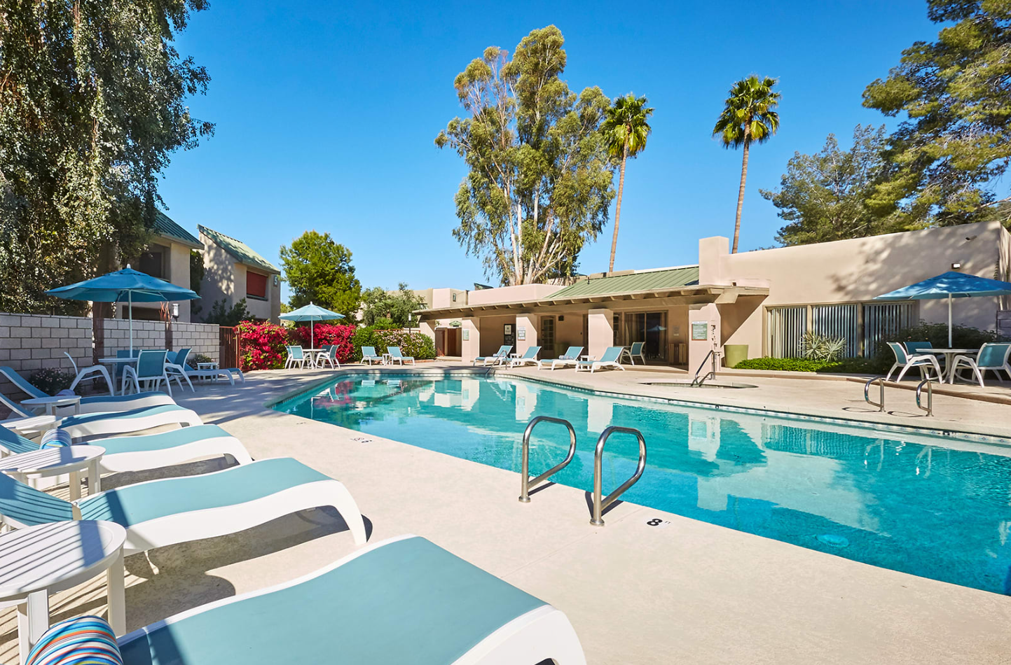 View of Soothing Blue Pool Surrounded by Blue Lounge Chairs in front of Resident Building