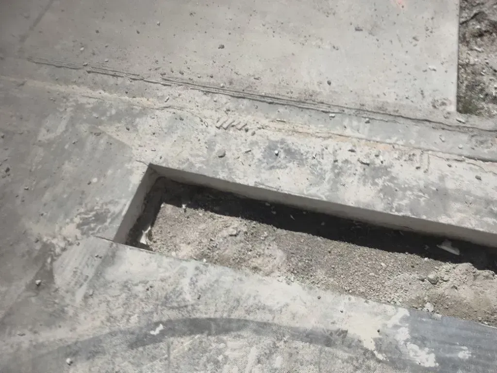 Concrete surface partially cut and removed, exposing trench with debris and dust, indicating demolit 