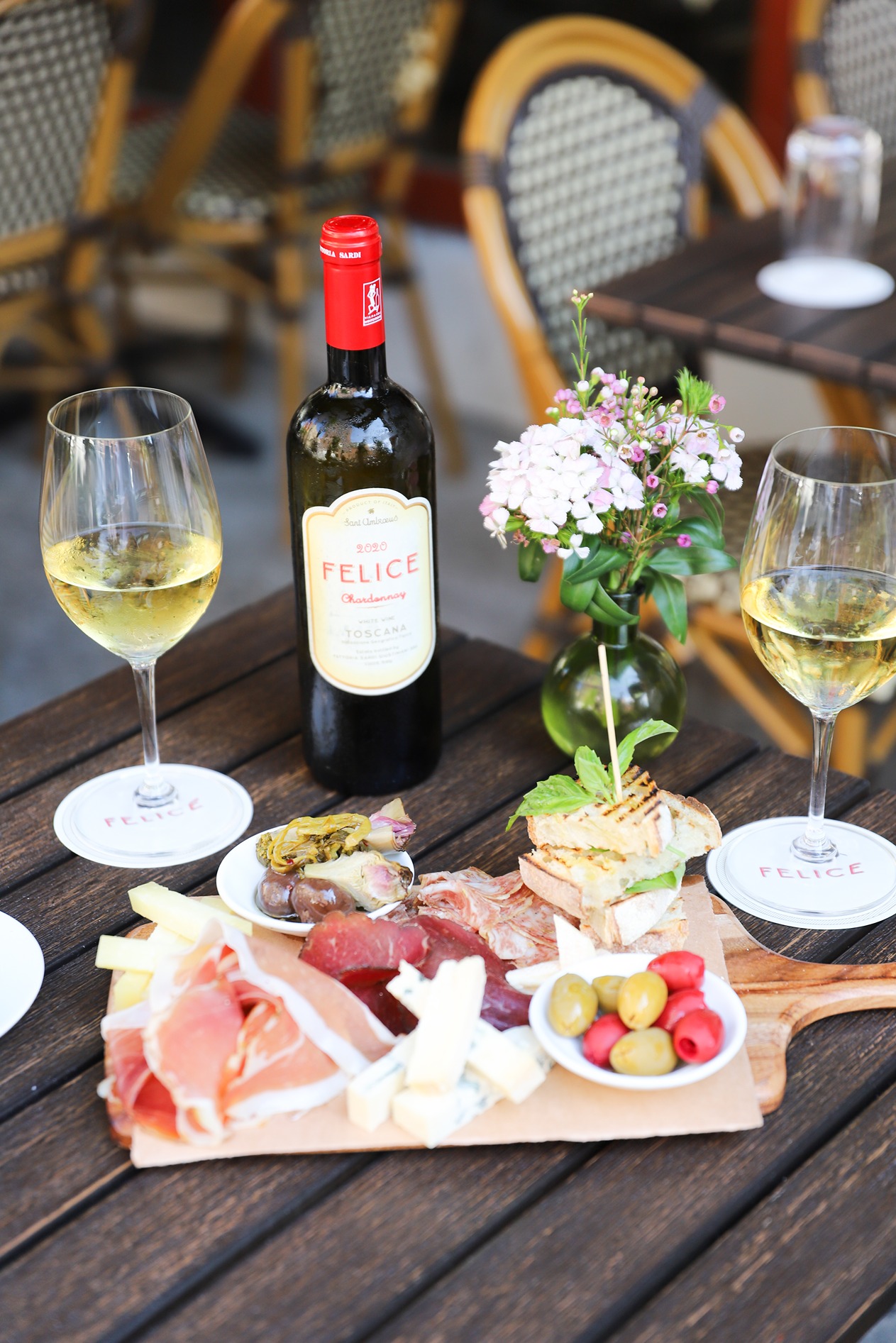 A bottle of private label Toscana Chardonnay sits next to an antipasto platter of cured meats, aged cheeses, olives, and panini.