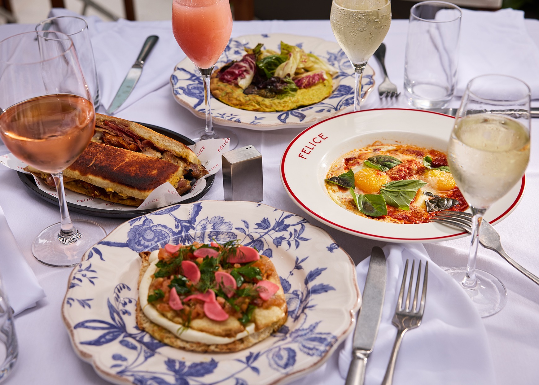 A delicious variety of breakfast and lunch options including Uova in Purgatorio, a toasted sandwich, and avocado toast, paired with glasses of ros&eacute; and sparkling wine.