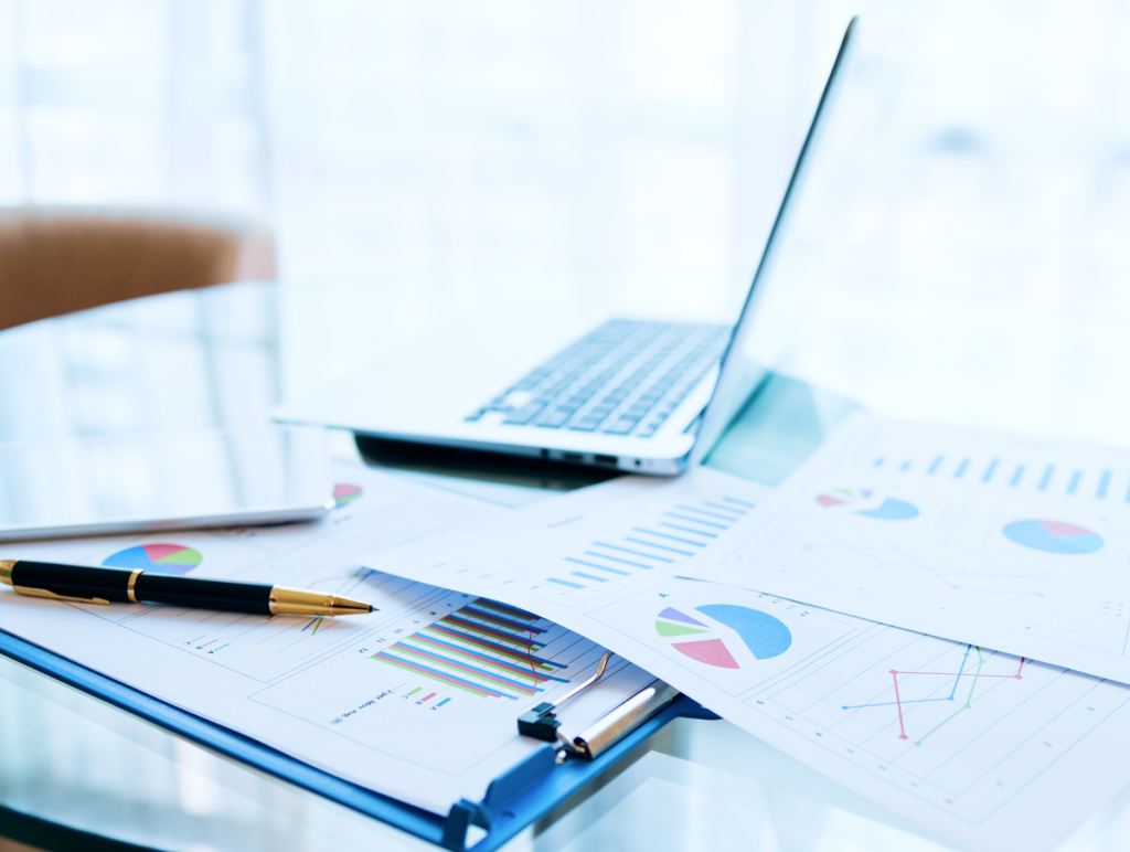 Close up of an office desk with a laptop and printed graphs.