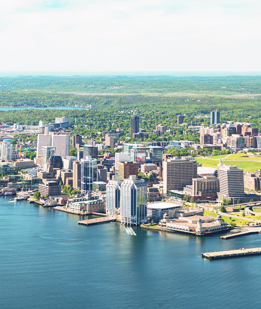 Aerial harbor cityscape with port cranes, waterfront buildings, and lush greenery.