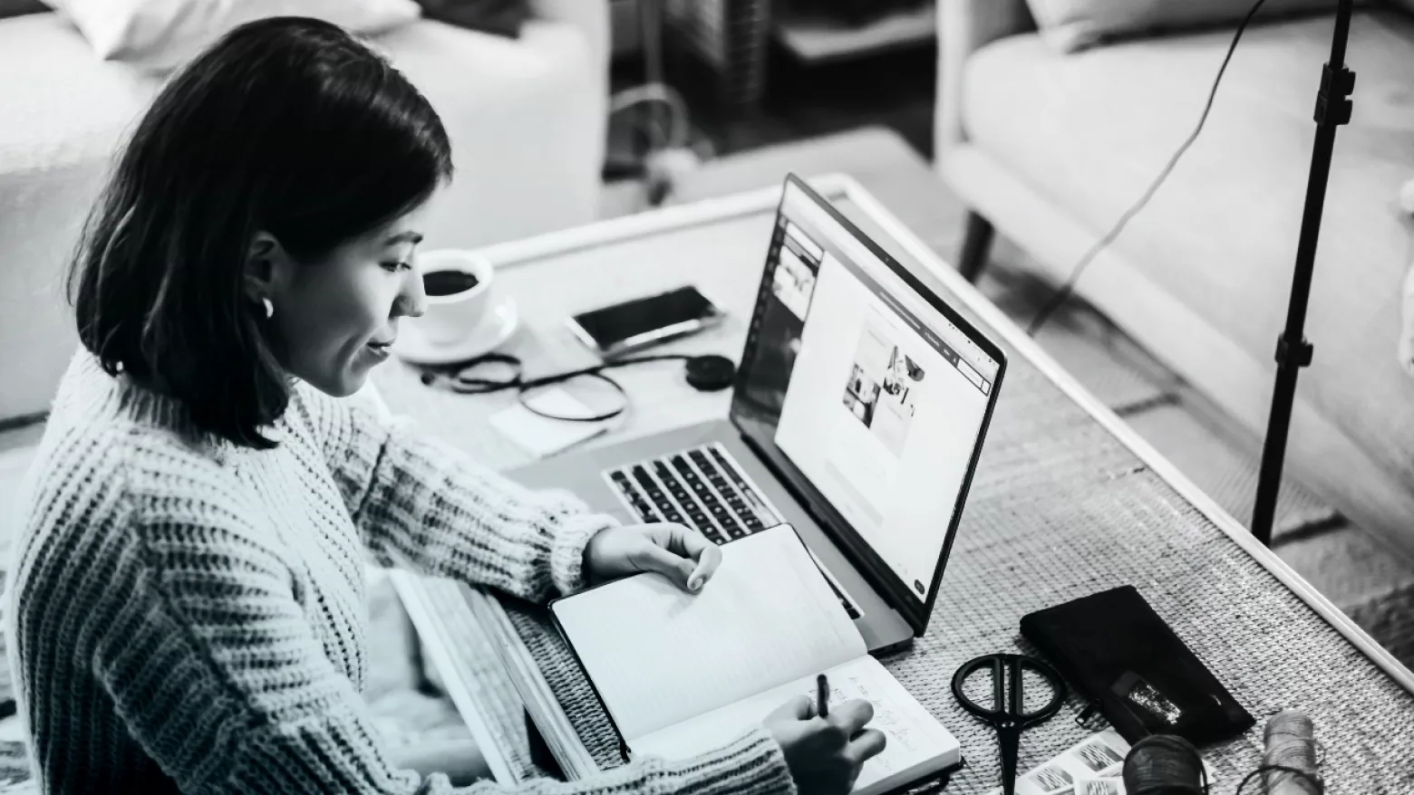 Woman sitting at a desk, writing in a book with a laptop open.