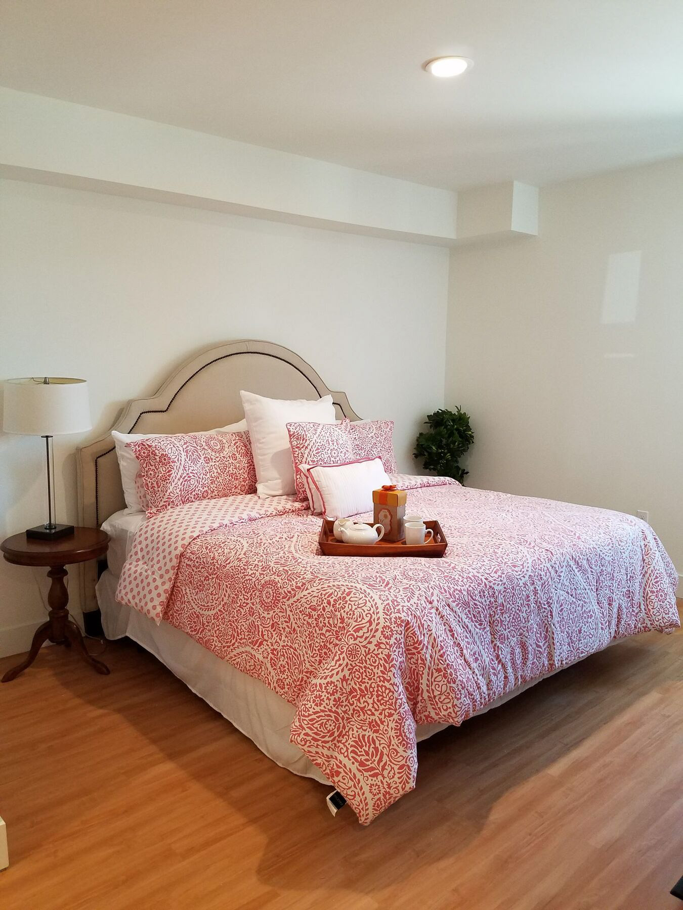 A bed with a red and white patterned comforter and matching pillow cases sits in a room with wooden flooring and white walls.