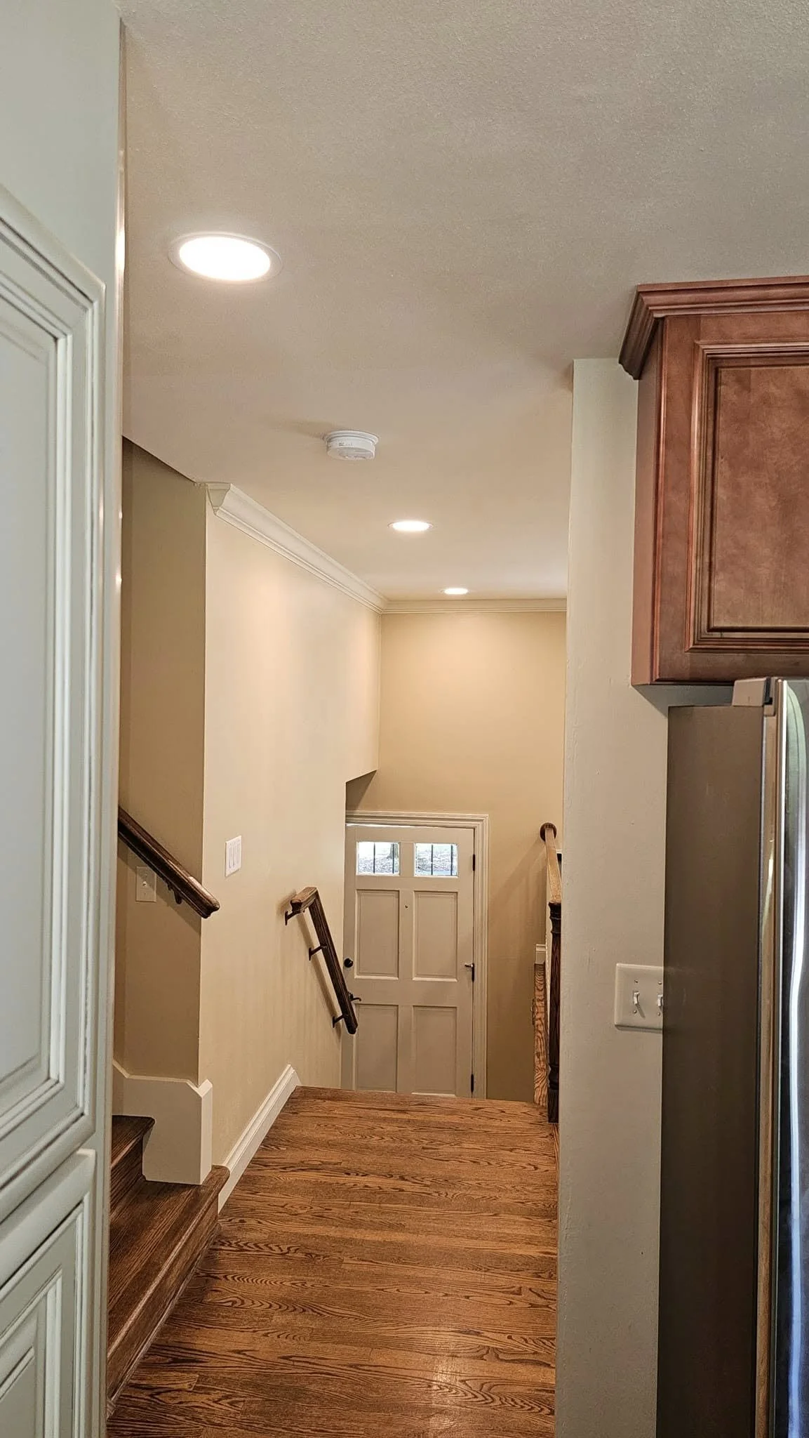 A hallway with wood floors and a white door at the end, with recessed lighting in the ceiling.