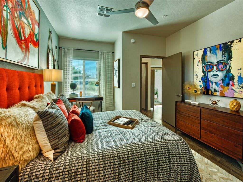 A bedroom with a bed with a grey comforter and a red bed frame. There is a ceiling fan and a window.