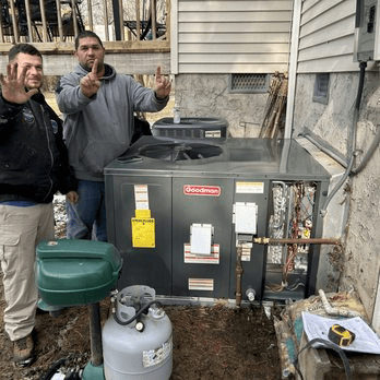 Technicians installing a Goodman residential HVAC system with outdoor condenser unit and propane connection.