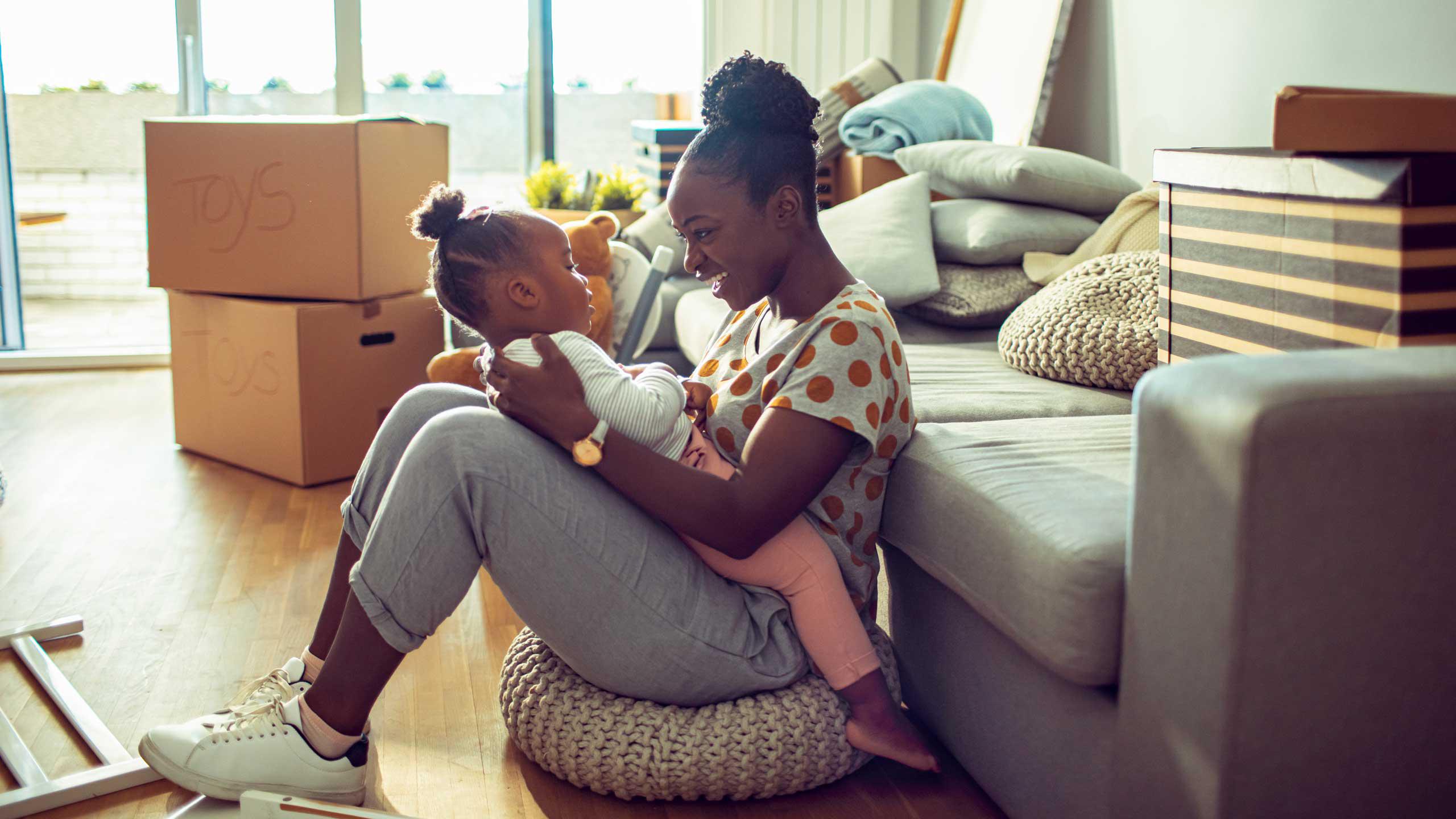 A woman in her apartment carrying her daughter and smiling