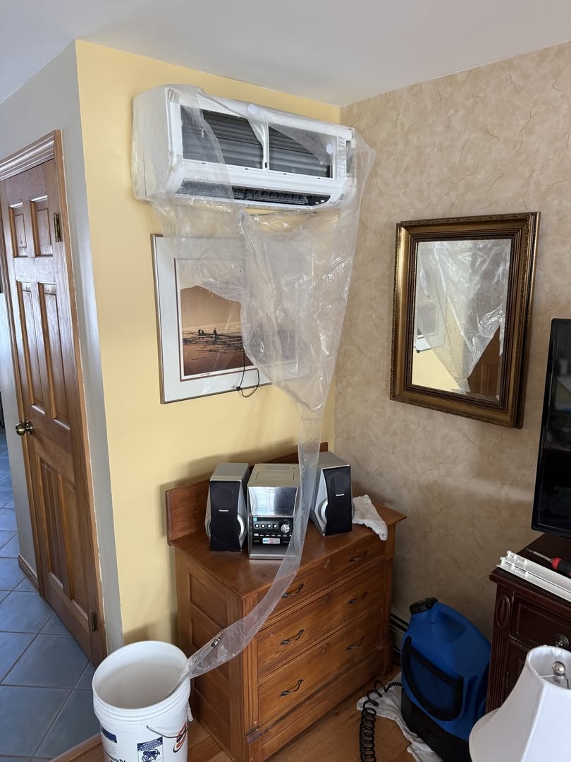 Professional heat pump cleaning performed by Upfront Home Inspection & Maintenance in Maine. A wall-mounted ductless mini-split heat pump is fitted with a protective cleaning bag to capture water and debris during the cleaning process.