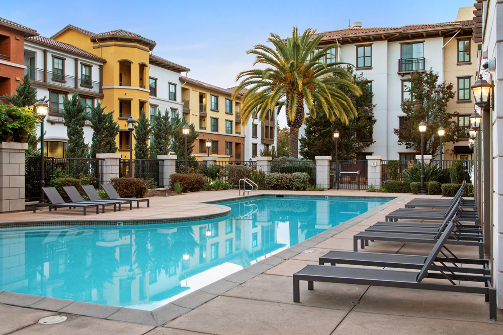 Pool with luxury landscaping, lounge seating, and view of Tuscan-inspired property exterior.