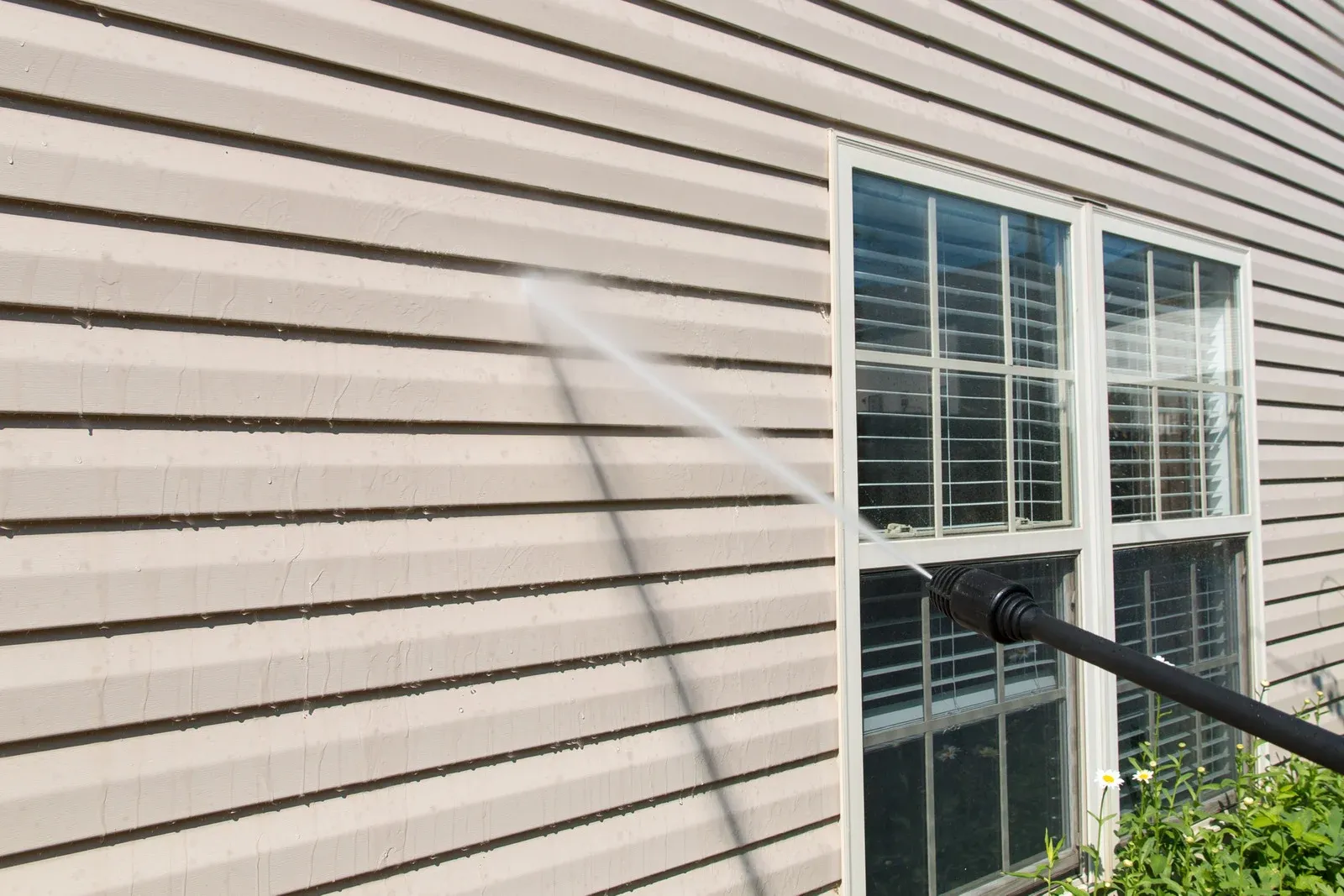 Pressure washing a home&rsquo;s exterior siding near a window, removing dirt, mold, and buildup. High-pressure water spray restores the surface&rsquo;s original look, enhancing cleanliness, improving curb appeal, and helping maintain the overall condition of the house exterior.