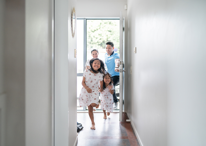 Parents and their two young daughters excitedly running down the front hall of their home.