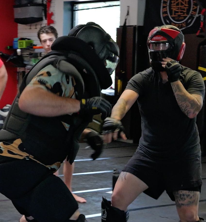 Two students in full protective gear during a high-intensity scenario drill on the mats.