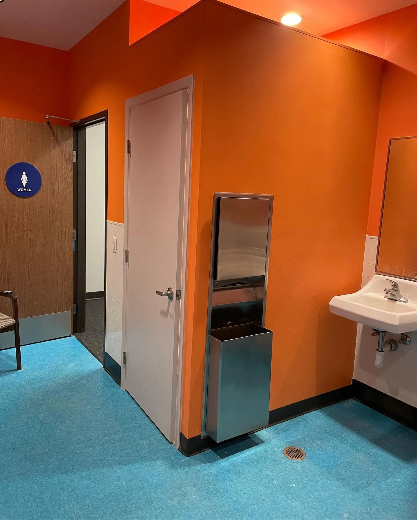 Commercial restroom renovation featuring freshly painted orange walls, updated sink, modern fixtures 