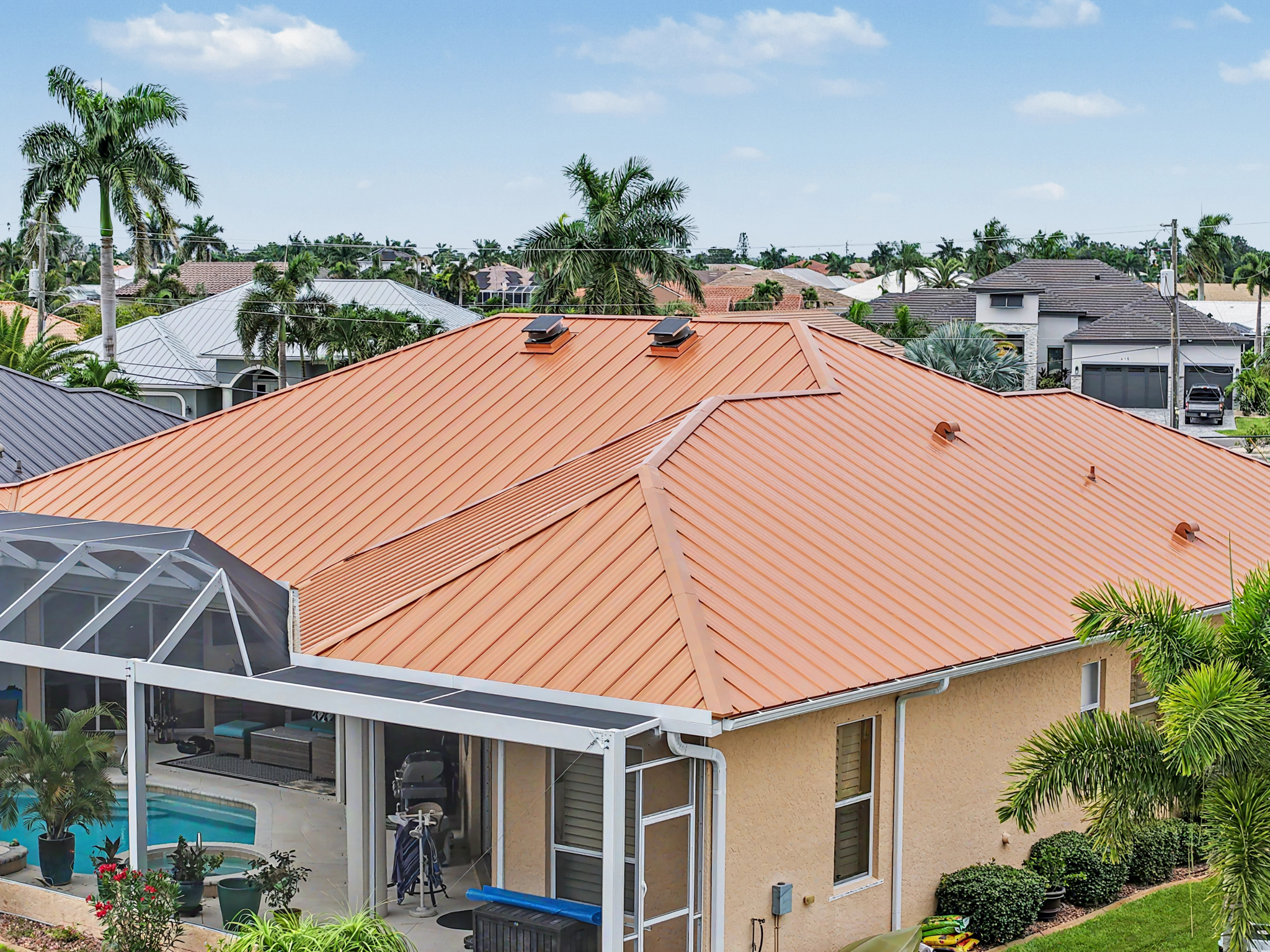 Rear aerial view of a coastal residence showing a copper-colored metal roof above a screened swimmin 