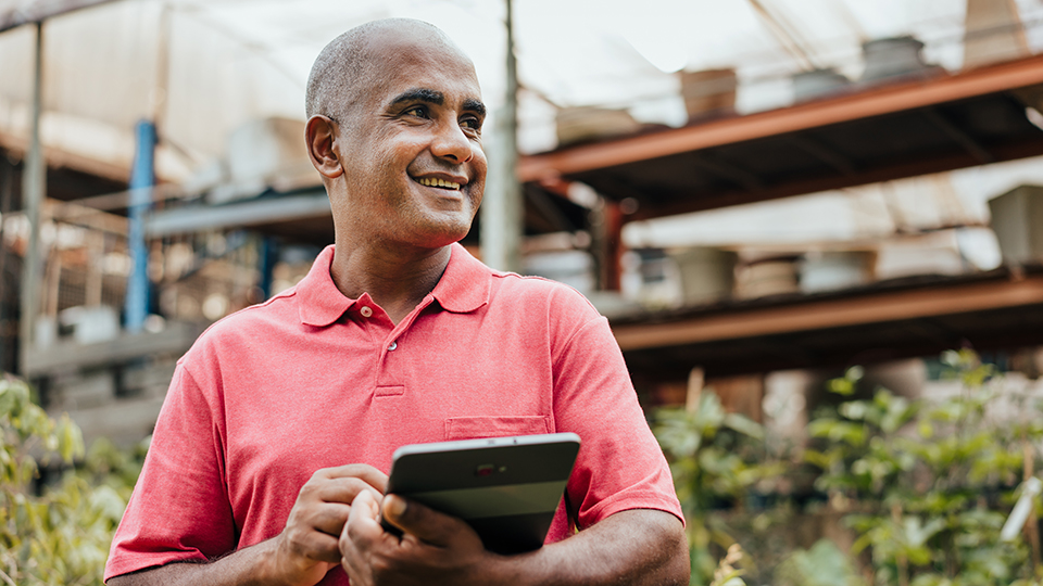 A man in a greenhouse holding a tablet