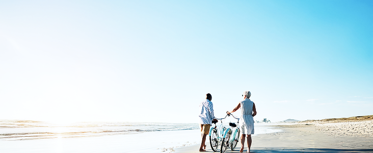 People walking with bikes on a beach.