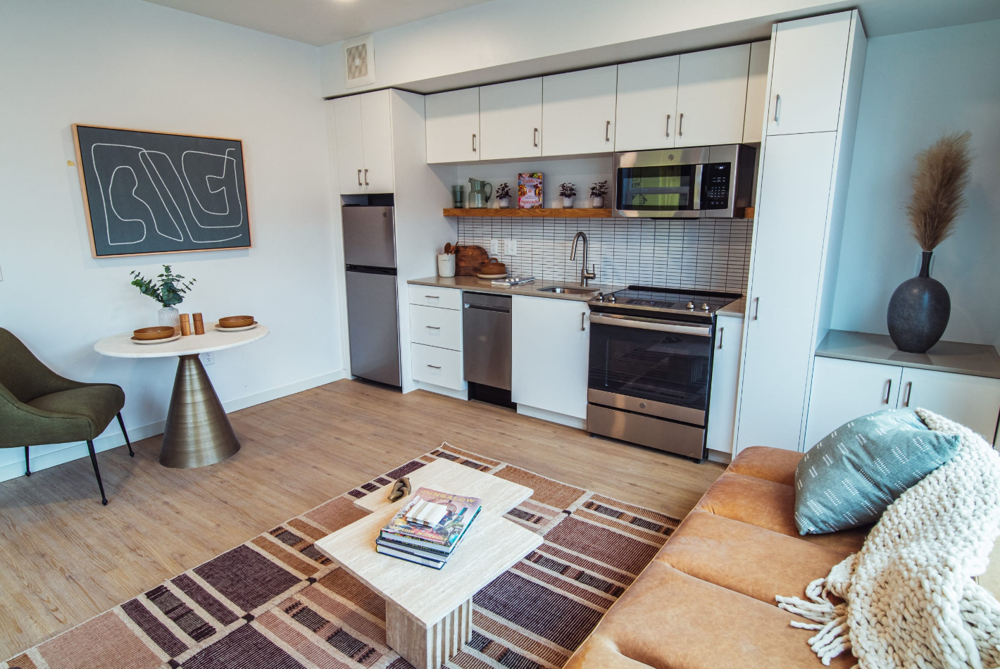 Kitchen and living room view with plank flooring, bistro-style dining area with a green accent chair, and modern abstract art above