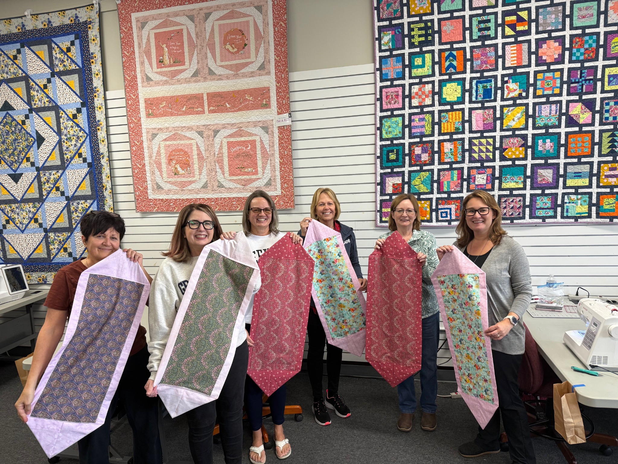 Students proudly display their finished table runner projects after a Decorative Stitch class. This hands-on quilting workshop focused on decorative stitching, precision piecing, and creating beautiful home décor.