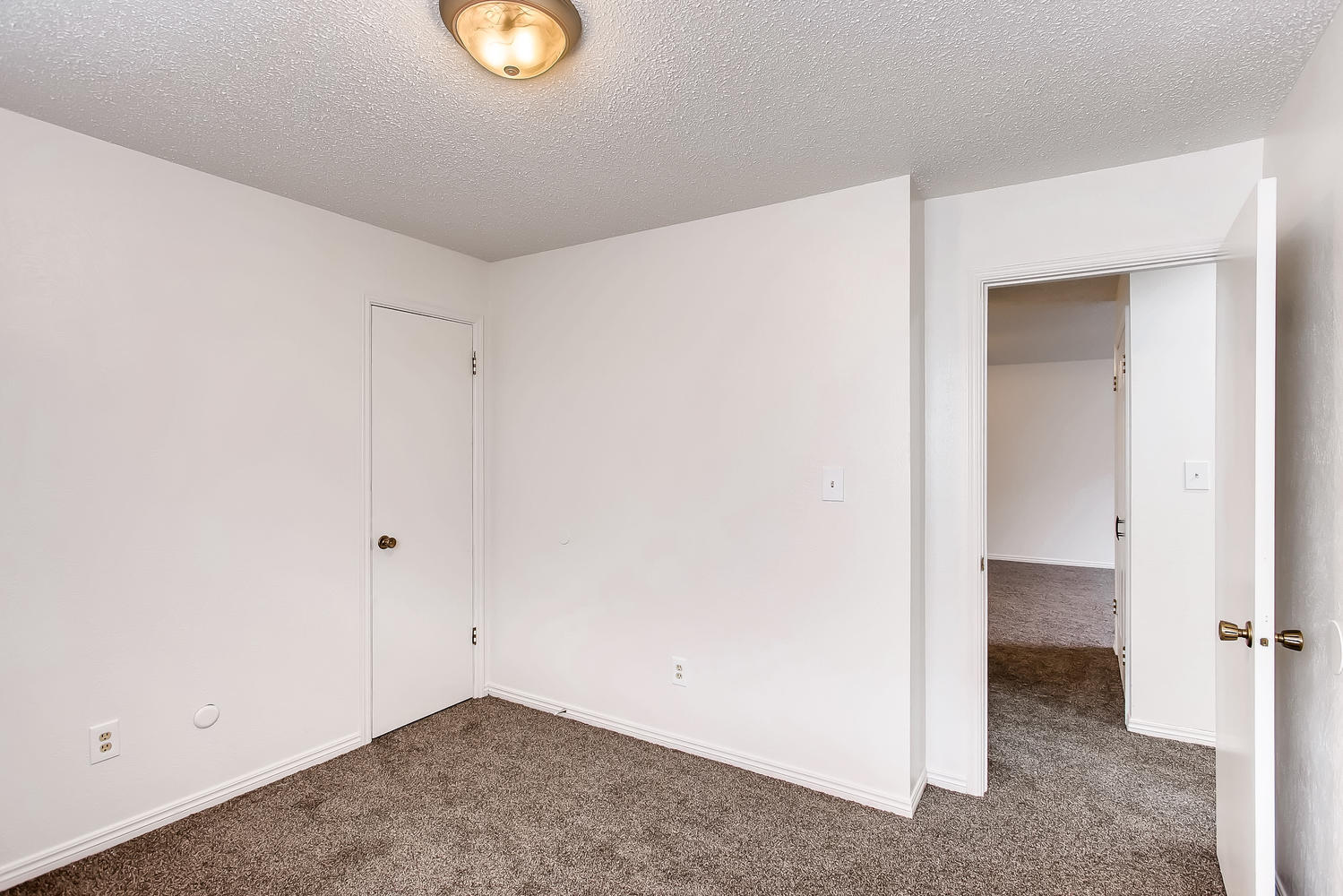 Carpeted bedroom with single light, door to bathroom, and door to hallway.