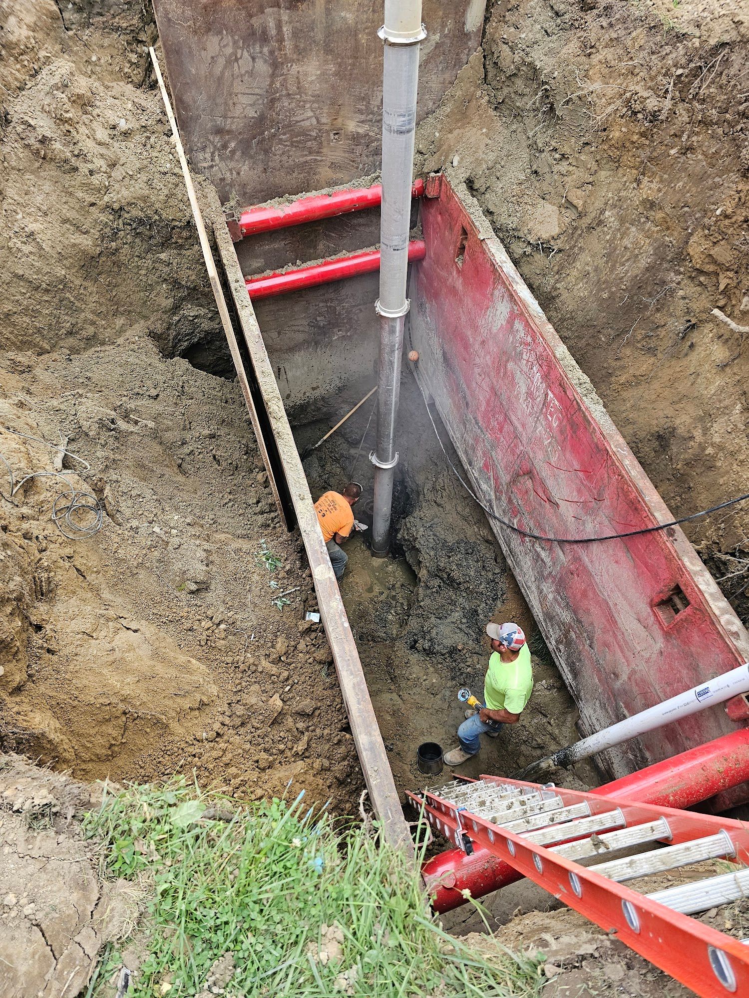 A crane lowers a precast concrete utility structure into a prepared excavation. Workers guide placement to ensure proper alignment for future utility and drainage connections.