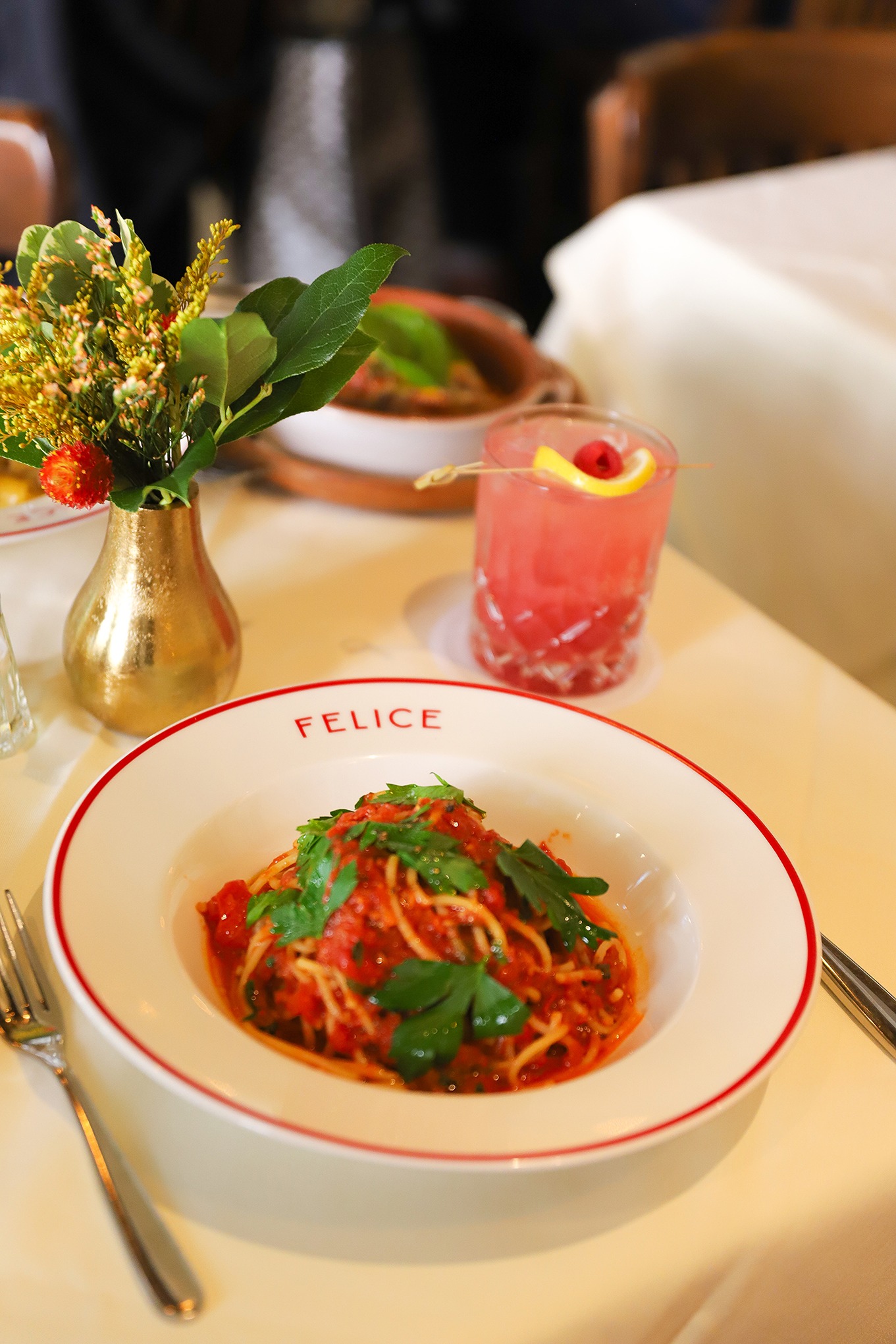 A classic Italian spaghetti dish with rich tomato sauce and fresh herbs, served alongside a refreshing raspberry garnished cocktail.