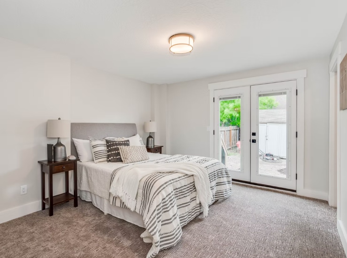 This bedroom is open, calm, and effortlessly inviting. Designed with a “Transitional Chic” style, it blends crisp white walls with warm, textured elements for a balanced look. A soft grey upholstered headboard and layered linen bedding add comfort and softness, while French doors bring in beautiful natural light. The result is a clean, relaxing space that feels both simple and refined. Let’s chat and bring your vision to life.