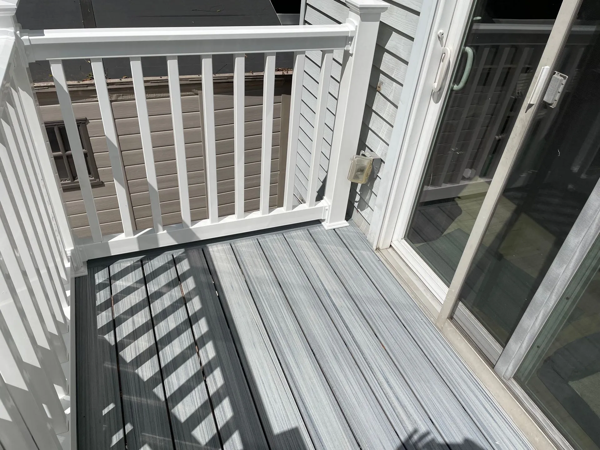Compact composite balcony deck with white railing and sliding glass door access. The low-maintenance outdoor area offers durability, safety, and a clean modern appearance for homeowners.