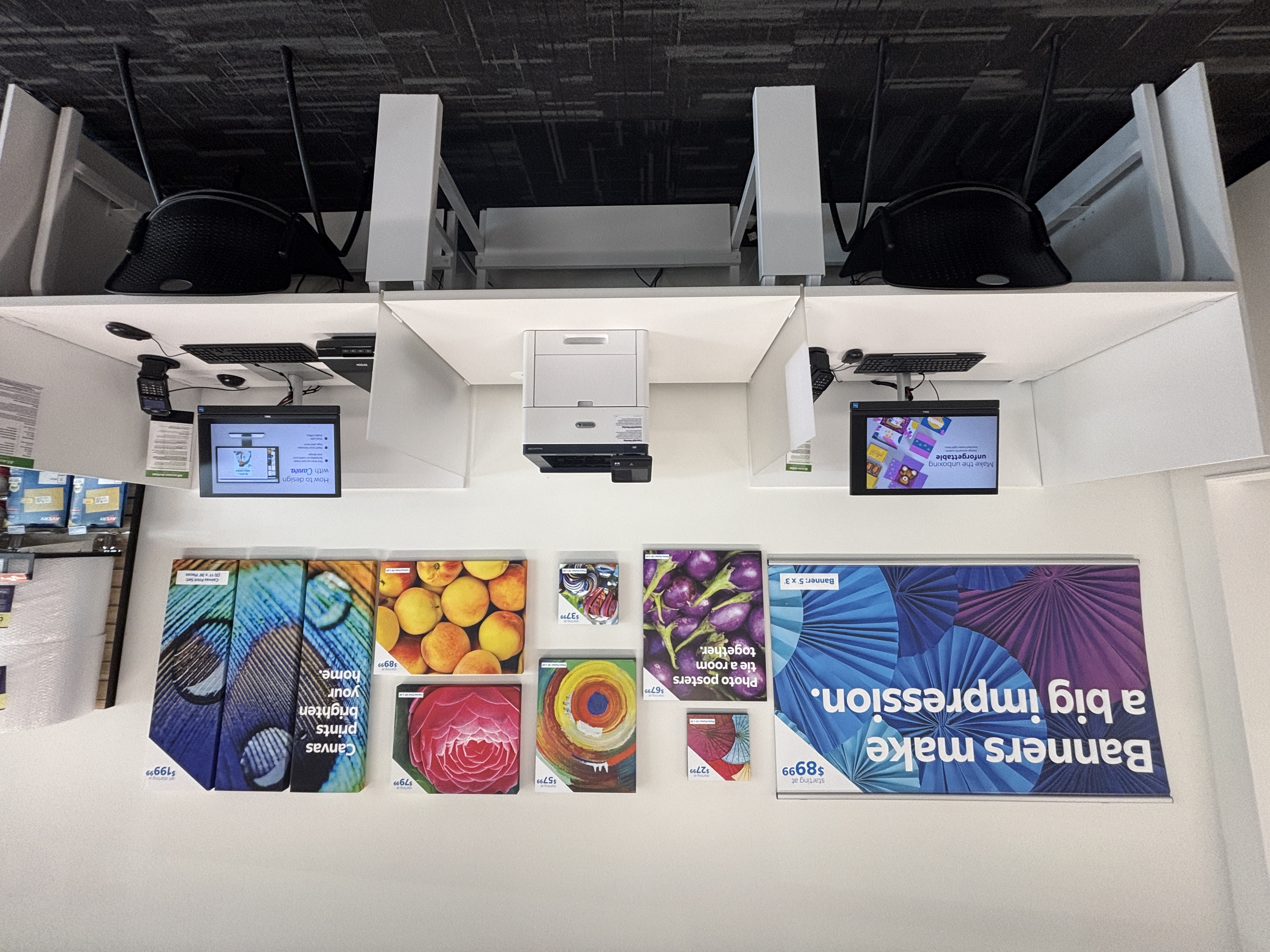 Self-service computer rental workstations and a display wall of custom print examples like banners and canvas prints.