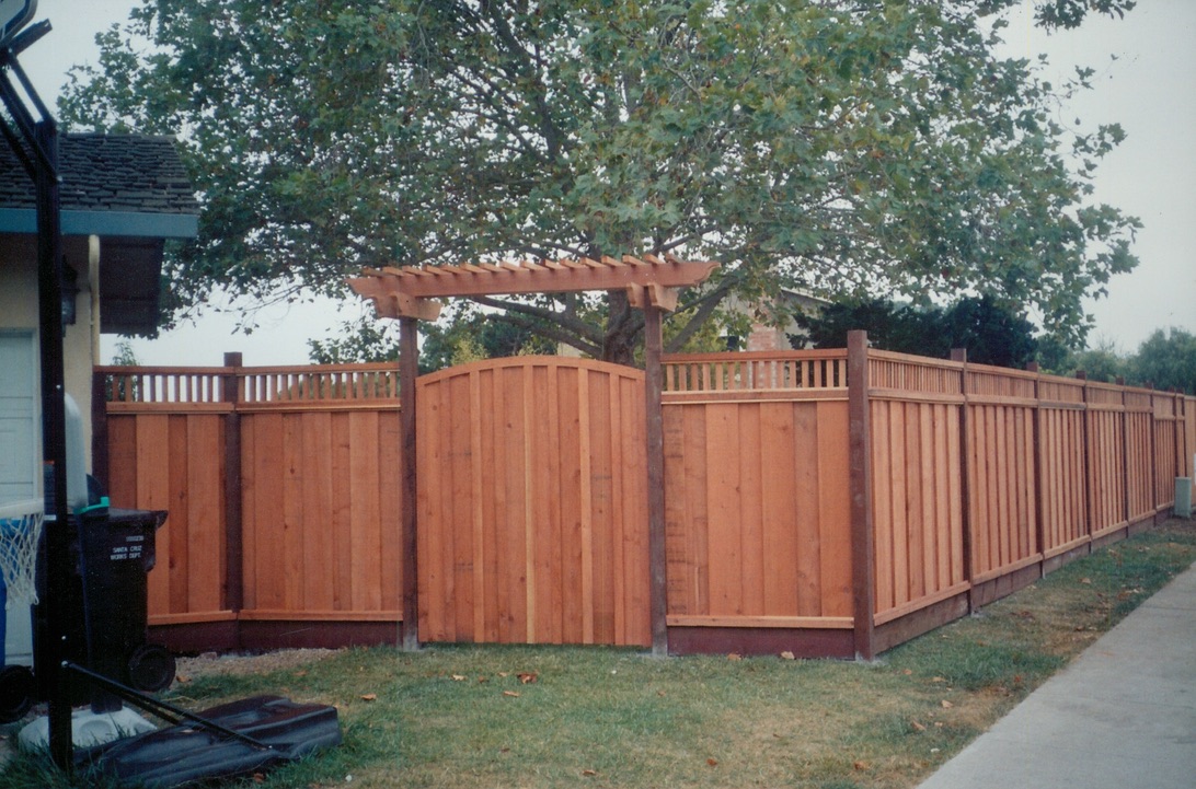 Wood privacy fence with decorative top trim installed around a residential yard for added security and curb appeal.