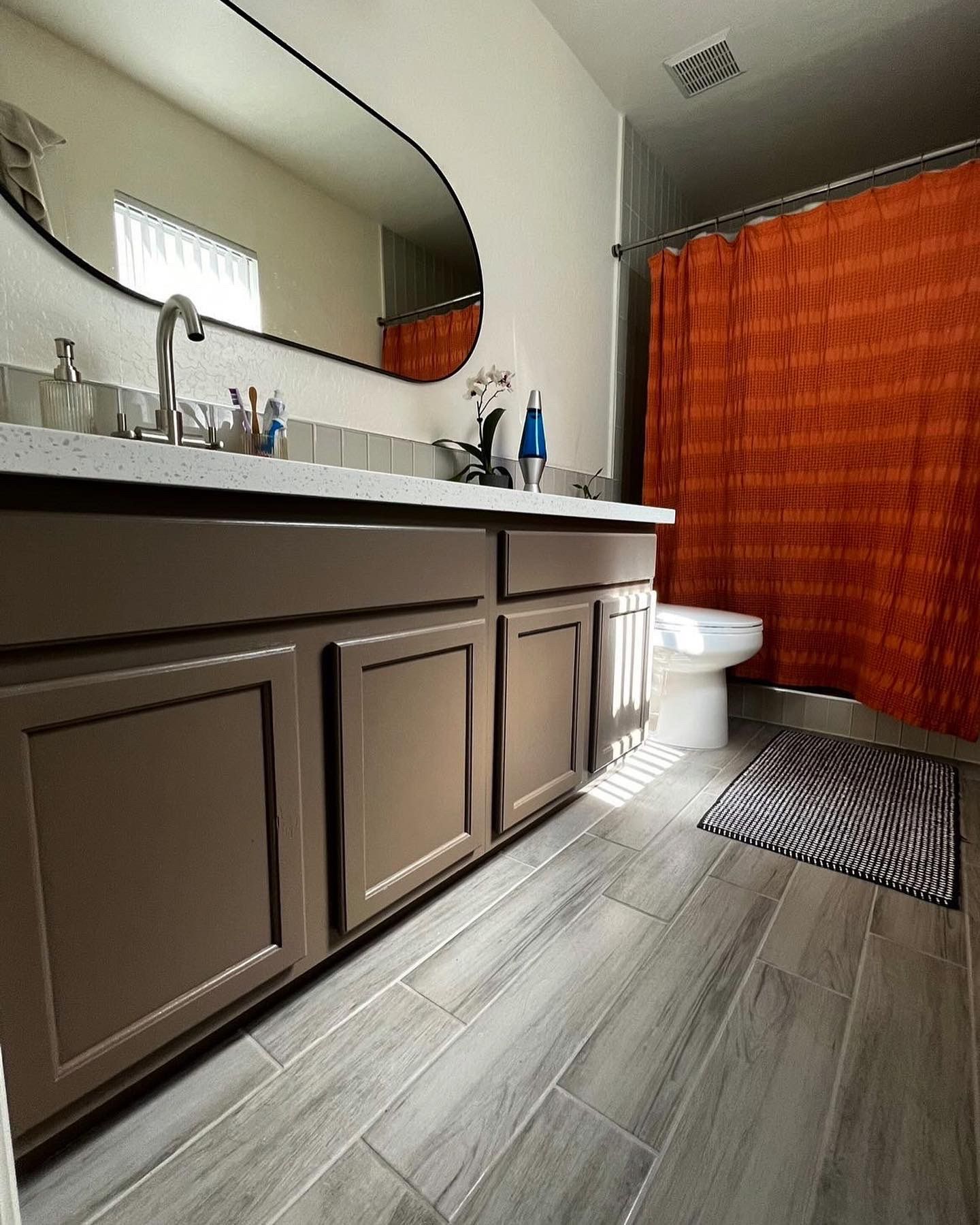 A modern bathroom features a sleek vanity with a large mirror, tiled flooring, and a bright orange shower curtain, combining clean design, functional layout, and contemporary interior styling.