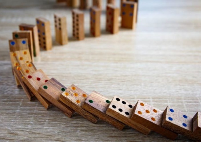 Line of dominoes beginning to fall on one another.
